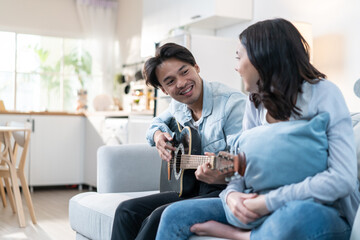 Asian young loving couple play guitar together in living room at home. 