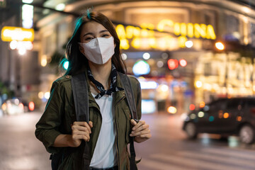 Asian attractive woman backpacker wear mask, walking in city at night. 