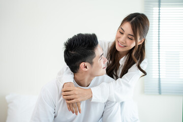 Portrait of Asian young couple sitting on bed and look at each other. 