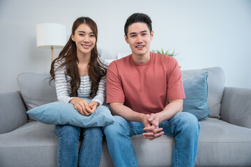 Portrait of Asian young loving couple sitting on sofa in living room.