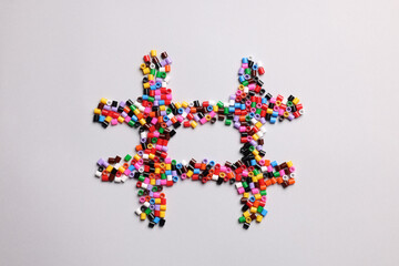 Hashtag symbol of colorful melty beads on light background, top view