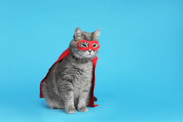 Adorable cat in red superhero cape and mask on light blue background, space for text