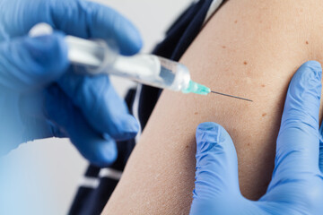 Medical worker injecting vaccine shot to patients shoulder, arm closeup detail - obrazy, fototapety, plakaty