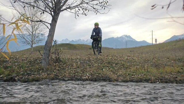The woman travel on mixed terrain cycle touring with bikepacking. The traveler journey with bicycle bags. Sportswear in green black colors. The trip in magical autumn forest, river stream.