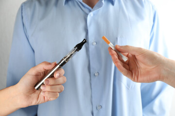 Man choosing between cigarette and vaping device on light background, closeup. Smoking alternative