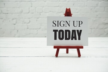 Sign up Today text and alarm clock on white brick wall and wooden background