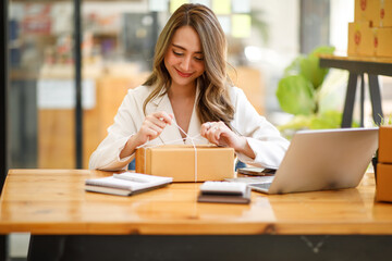 	
Startup SME small business entrepreneur SME or freelance Asian woman using a laptop with box, Young success Asian woman with her hand lift up, online marketing packaging box and delivery, SME concep