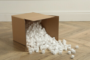 Overturned cardboard box with styrofoam cubes on wooden floor indoors