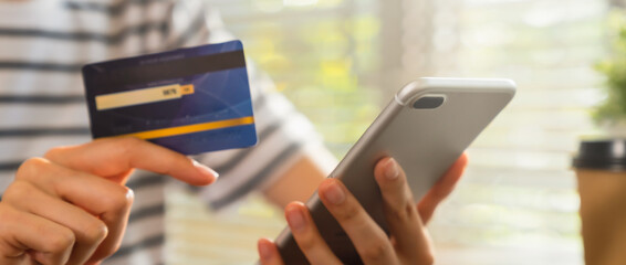 Close-up of hand holding credit card and using smartphone with online payment for shopping.
