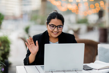 A young Indian woman is holding a video conference sitting in a cafe on the terrace. Freelance,...