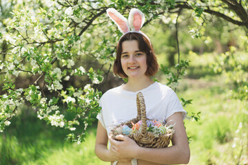 Easter egg hunt in spring garden. Funny teen girl with eggs basket and bunny ears on Easter egg...