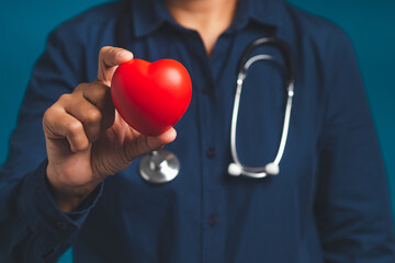 Hand of a doctor holding a red heart shape while standing on a blue background