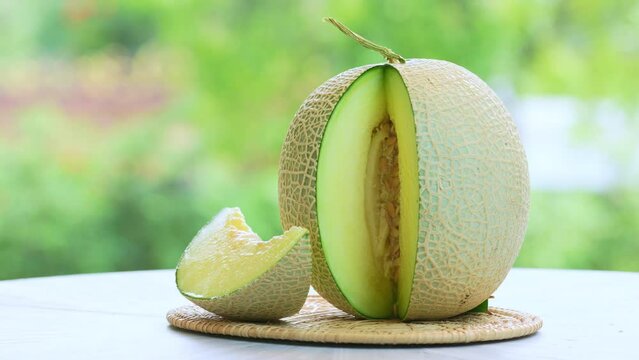 Green Melon on blurred greenery background, Cantaloupe Melon fruit in Bamboo mat on wooden table in garden.