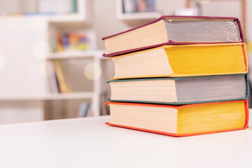 Thick old books with colorful covers lie in pile on white office table against backdrop of bookshelf.