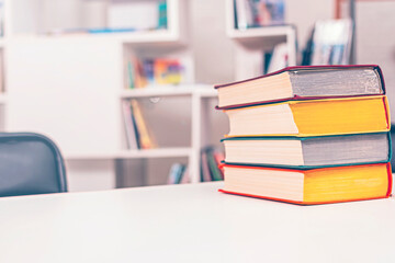 Stack of old thick multi-colored books lies on white office table. In background is bookshelf.
