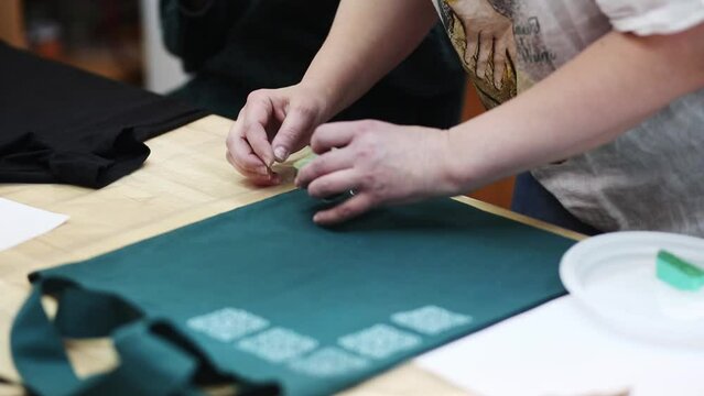Hand-printed pattern on fabric. Women's hands put a seal on the shopping bag. Ancient traditions. Modern hobbies and creativity.