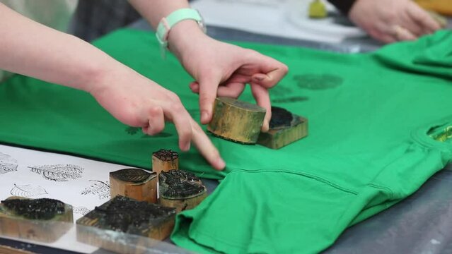 Hand-printed pattern on fabric. Women's hands put a seal on a green T-shirt with acrylic paints for fabric. Ancient traditions. Modern hobbies and creativity