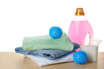 Dryer balls, detergents and stacked clean clothes on wooden table against white background