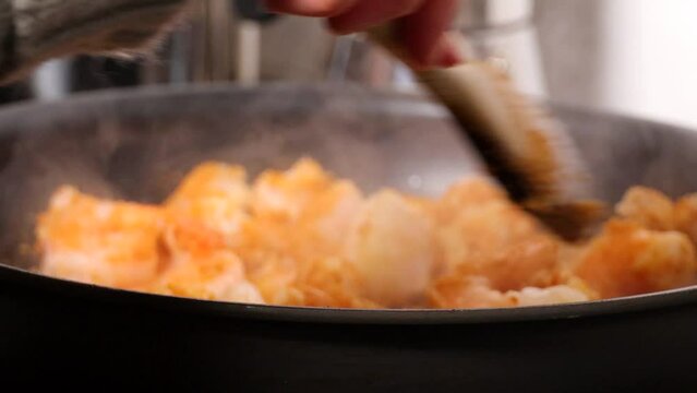 A cook fries white codfish and shrimp in a frying pan