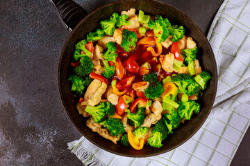 Spicy chicken teriyaki with broccoli in pan on dark background.