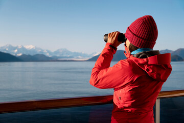 Alaska Glacier Bay cruise ship passenger looking at Alaskan mountains with binoculars exploring...