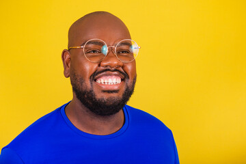handsome afro brazilian man wearing glasses, blue shirt over yellow background. closeup photo...