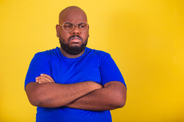 handsome afro brazilian man wearing glasses, blue shirt over yellow background. arms crossed,...