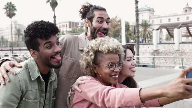 Group of multiracial young friends making funny faces while taking selfies on mobile phone - Millennial people having fun with new social media trends. High quality 4k footage