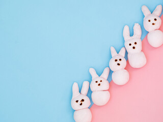 White handmade marshmallow candy bunnies on bicolor blue pink paper background with copy space for your Easter text message. Minimal happy Easter holiday conceprt. Top view flat lay.