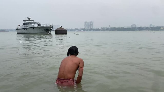 Close up view of male taking a dip in the ganges river at sunrise in Kolkata,India with the view of boat in the background.