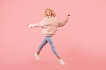 Fototapeta na wymiar Joyful stylish woman running and jumping, posing in mid-air over pink studio background, copy space