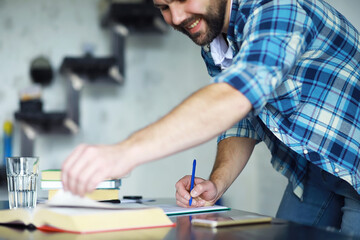 Portrait of joyful young man reading book in his living room.Student holding and reading book.