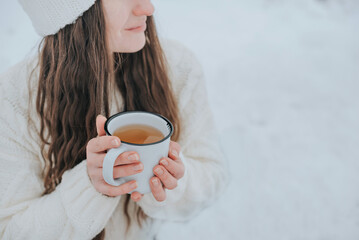 Female hands hold a drink in a white mug.