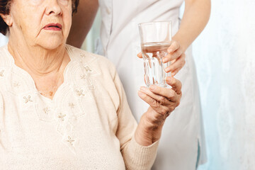 A nurse gives a glass of water to an elderly woman. Care for the elderly in nursing homes