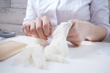 Professional manicurist puts on white medical gloves. Preparing for customer service in nail beauty salon.