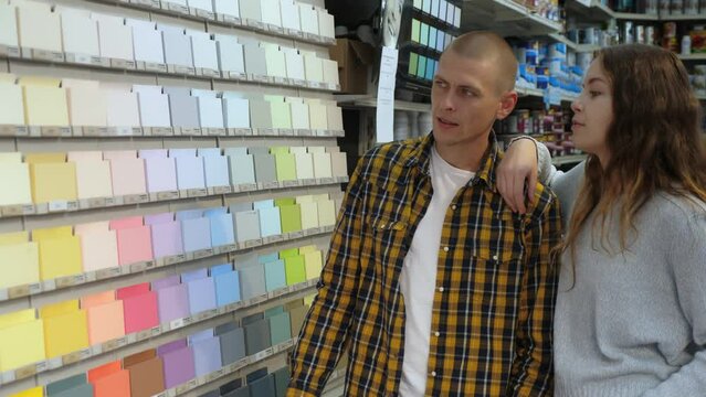 Couple of positive customers choosing together paint color for renovation works in a hardware store