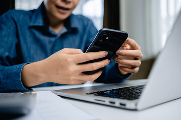 Close up of Businesswomen using a smartphone and laptop computer with analyzing business report graph and finance chart at the workplace, financial and investment concept.