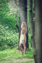 Fototapeta na wymiar Blonde girl in a light airy dress, barefoot at dawn in a summer forest