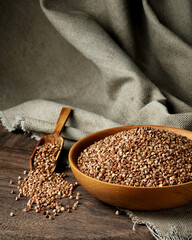 Organic buckwheat groats in a wooden bowl with a spoon on a linen napkin on a wooden table. Banner. Rustic style. Healthy nutrition concept. Buckwheat contains a large amount of vitamins and minerals.