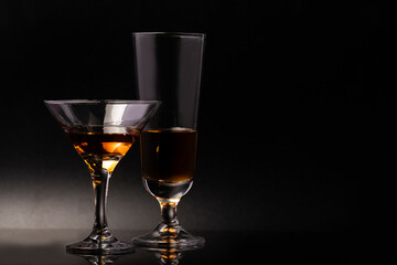 Two glass glasses on a beautiful leg with an alcoholic drink on a black background. - 487028032
