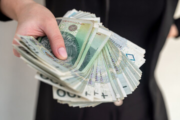 Young woman smiling happily, holding Polish zloty banknotes in the city.