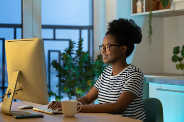 Young happy african woman freelancer in glasses working remotely in cozy home office with...
