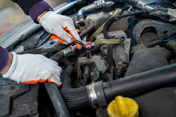 a man in gloves looks under the hood of an open car for a breakdown.