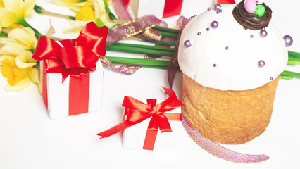 Easter cakes with narcissus flowers and gift box on white table.