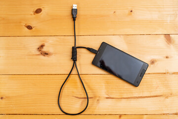 hangman noose made from an usb cable, connected to a generic smartphone, on wood boards background, representing social media depression