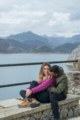 Pareja joven enamorada sentada y abrazada en un banco con las montañas nevadas de fondo