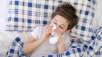 Child cold flu illness tissue blowing runny nose. toddler boy is lying in bed and blowing nose into...
