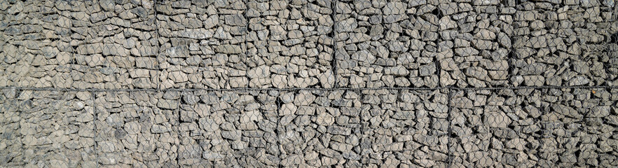 grey stone and pebbles in wire mesh wall horizontal stones facade background in panoramic web header