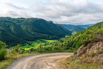 Obraz premium Piękna dolina Courgoul oświetlona promieniami słońca, położona pośród gór, w tle pasmo górskie Sancy pokryte chmurami