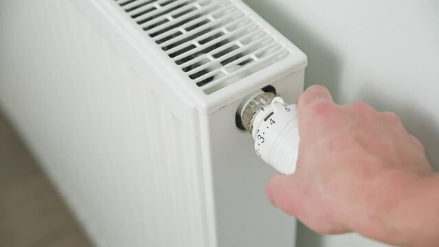 Hand adjusting temperature on heating radiator thermostat, Turning heat radiator knob to control heat in home
